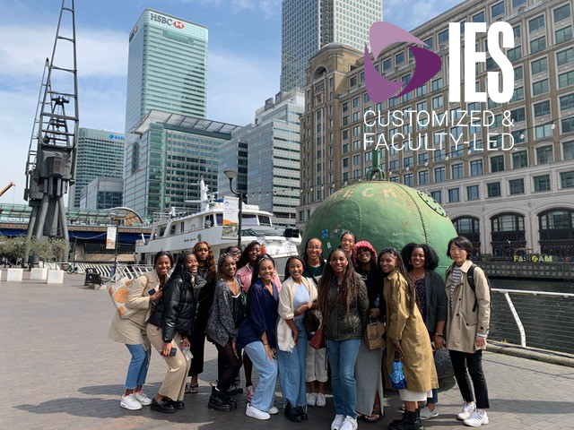 Group of students smiling in front of sphere statue.
